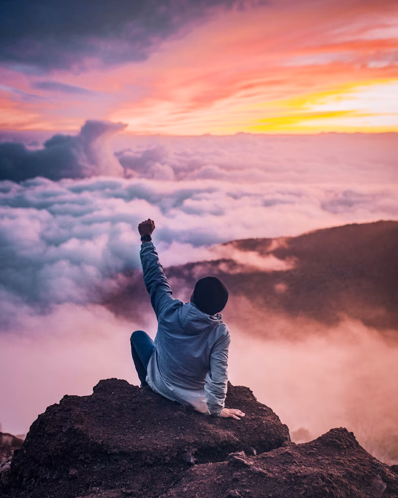 Confident person raising arms atop a mountain at sunrise, symbolizing personal growth, self-belief, and empowerment.